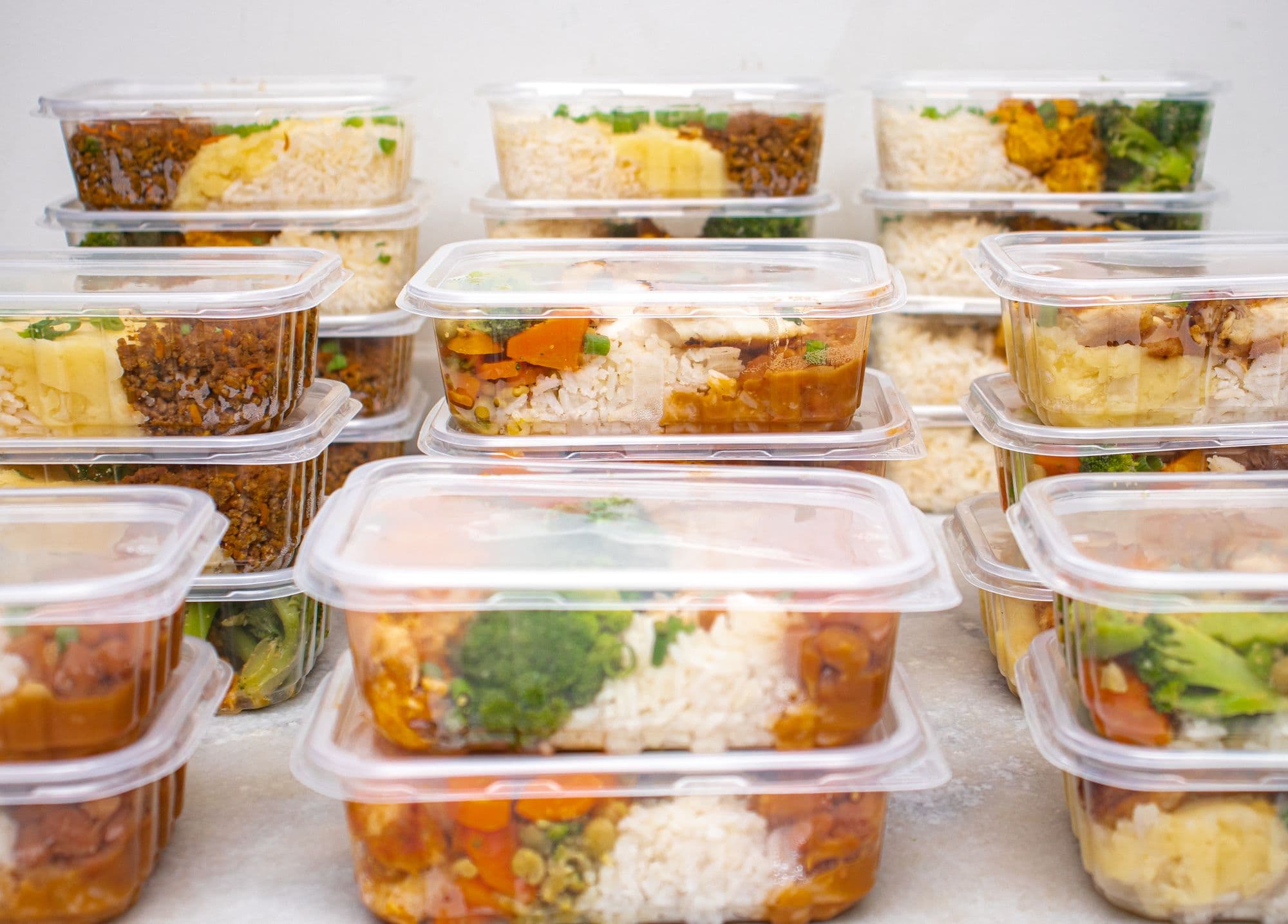 Sealed meal-prep containers stacked and ready to go out, each with rice, vegetables and a protein