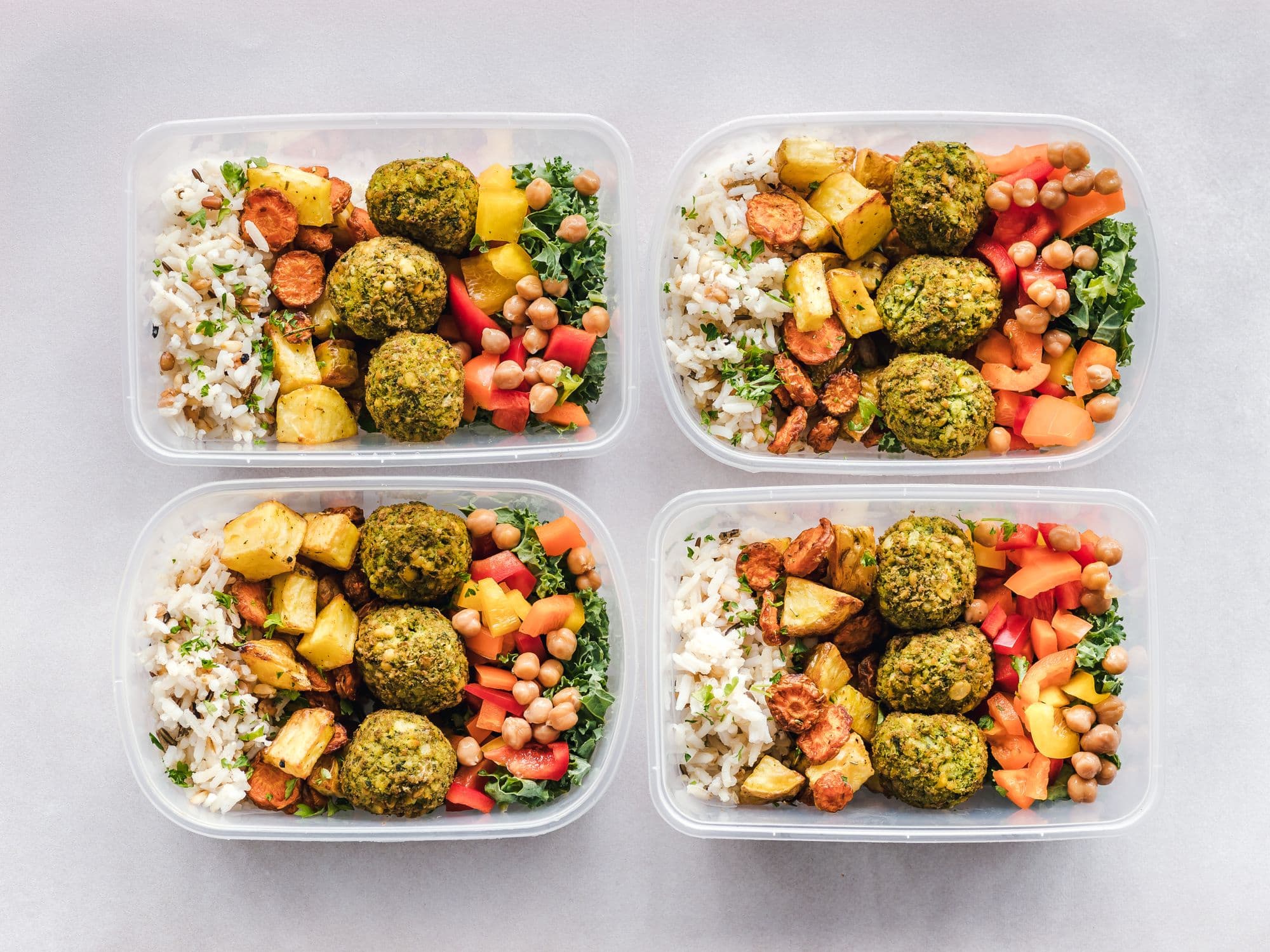 Four meal-prep containers laid out in a grid, each with rice, roast vegetables, peppers, kale and chickpeas
